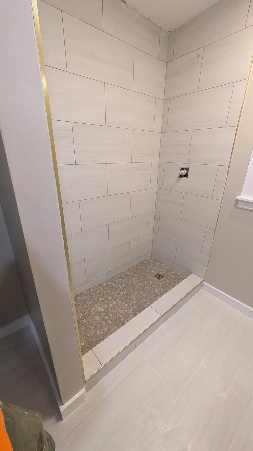 Tile shower with light rectangular walls and a mosaic floor